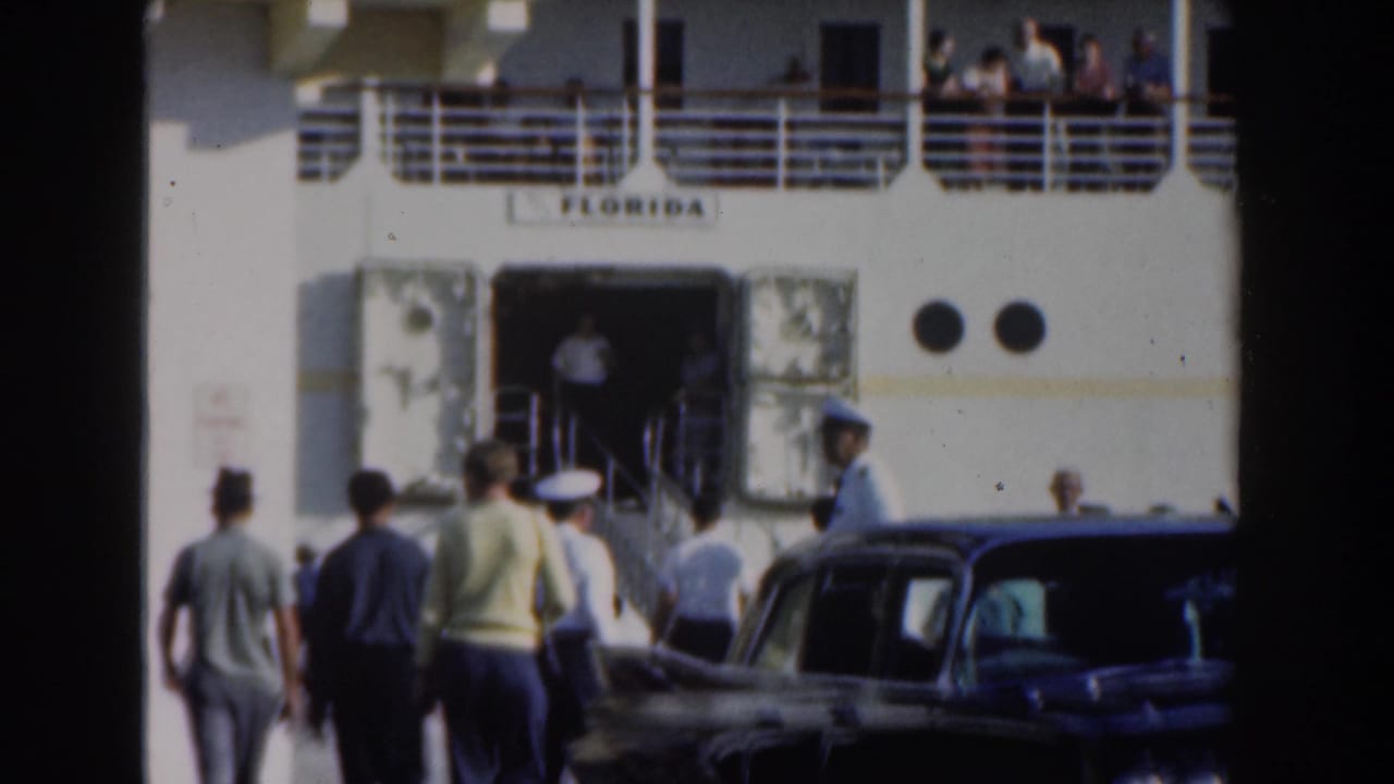 1961 Nassau home-movie frame showing people approaching the cruise ship Florida, with cars, a gangway entrance, portholes, and passengers on deck.
