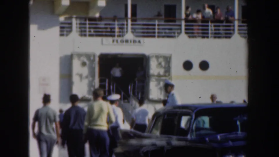 1961 Nassau home-movie frame showing people approaching the cruise ship Florida, with cars, a gangway entrance, portholes, and passengers on deck.