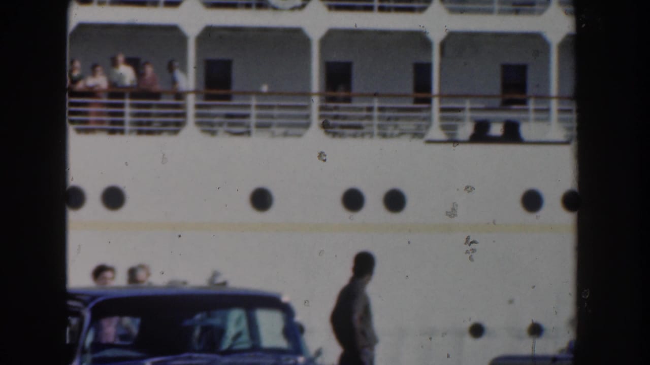 Upper decks and portholes of a white cruise liner with passengers at the rail.