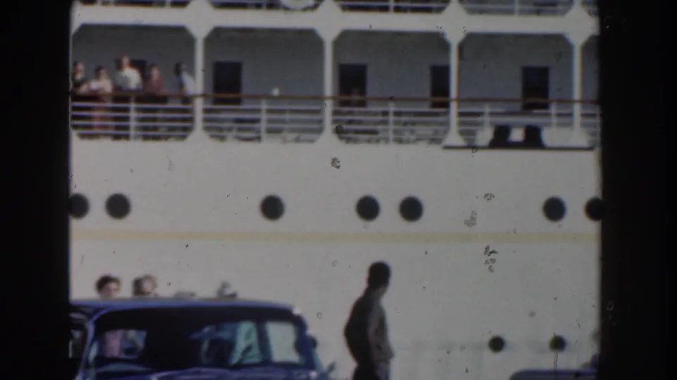 White cruise liner in Nassau with passengers gathered along the upper rail and round portholes visible on the hull.