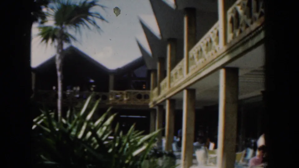 Nassau port-side frame showing a palm, balcony railings, shaded structures, and bright tropical light near the cruise area.