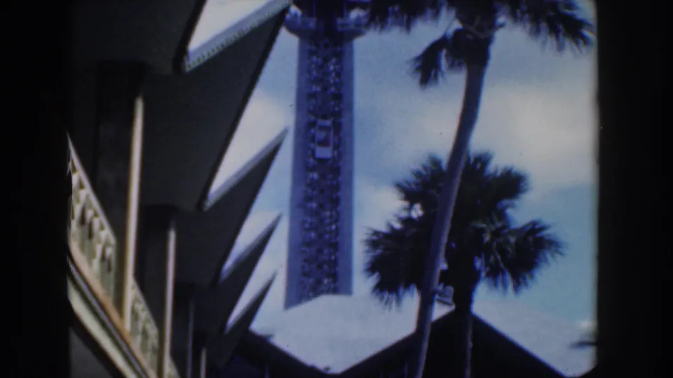 1961 Nassau home-movie frame showing an observation tower with palms and modernist rooflines in the foreground.