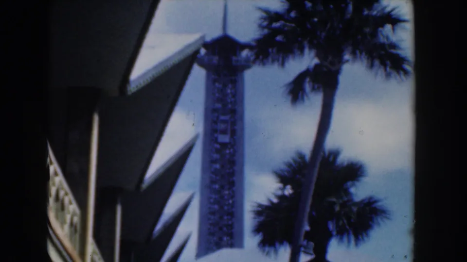 Nassau 1961 8mm frame showing the observation tower and elevator car partly framed by palms and foreground architecture.
