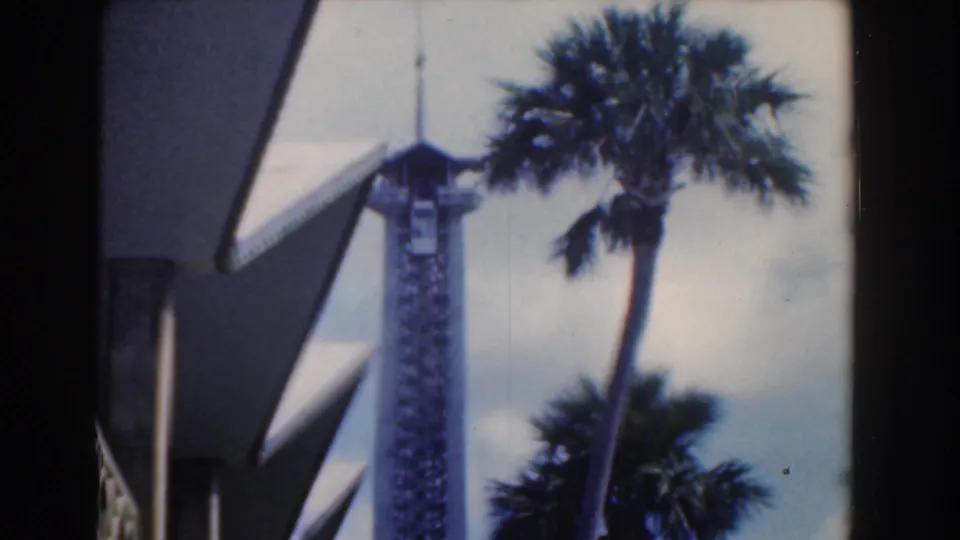 1961 Nassau home-movie frame with softened focus on a white tower, palms, bright sky, and angular architecture.