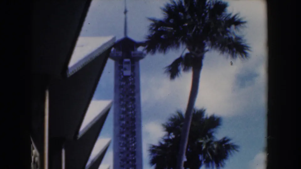 1961 Nassau frame showing a white observation-style tower framed by palms and dark angular foreground architecture.