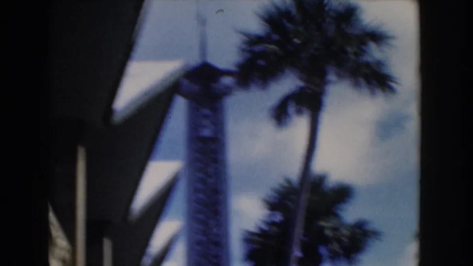 Soft 1961 Nassau frame with a tall tower, palm trees, sky, and shaded modern roofline.