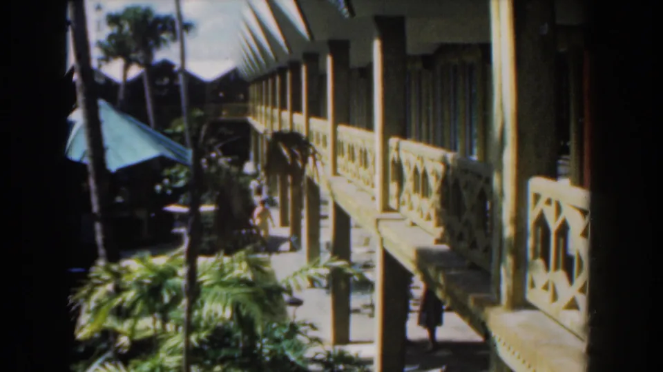 The final 1961 Nassau frame holds on the open-air building exterior, with palms, balcony railings, and partly visible people in shadow.