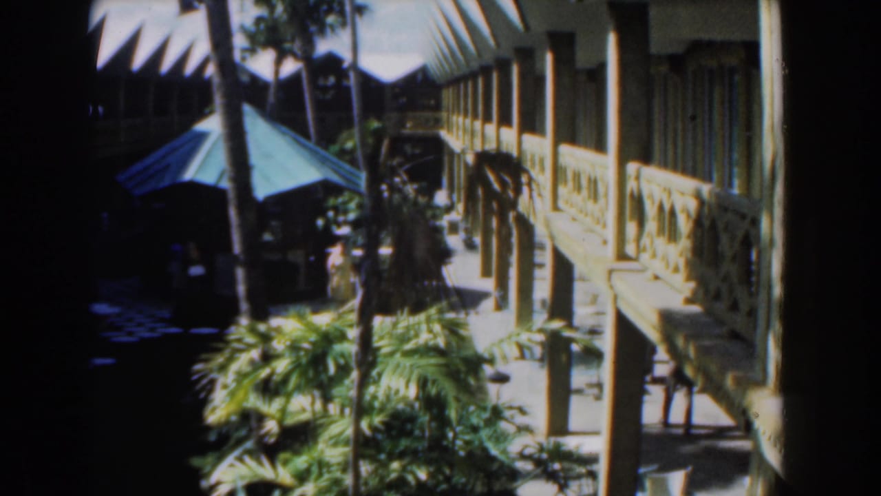 Courtyard walkway beside a two-storey building, with palms and a blue canopy.