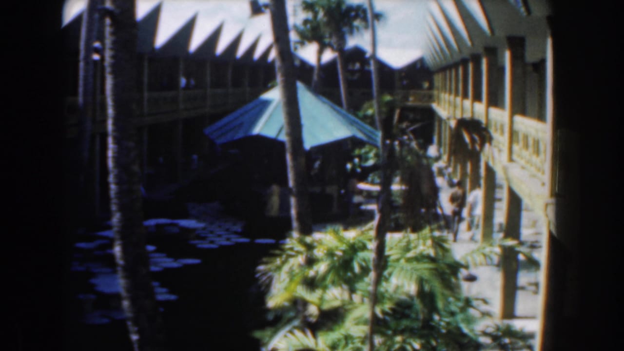 Palm-lined courtyard with a blue umbrella and two-story building in the background.