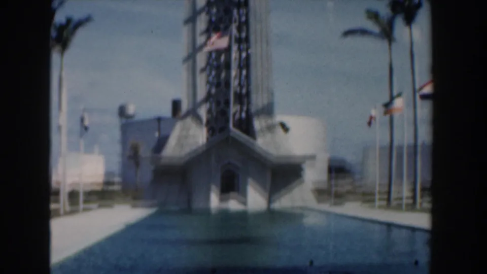 1961 Nassau frame with a central angular building, still pool water, flagpoles, palm trees, and soft faded 8mm color.