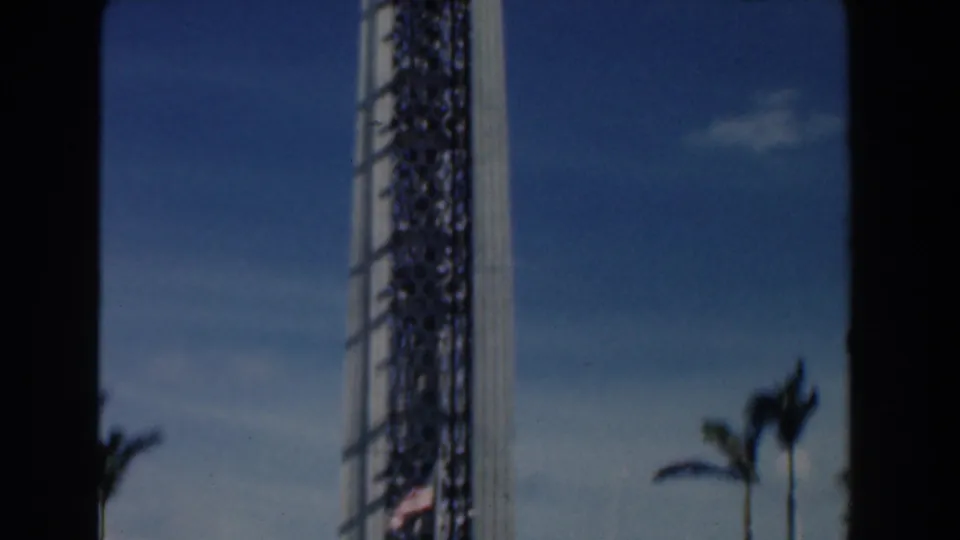 1961 Nassau frame with the camera tilted upward along the tower, showing palms and open sky.