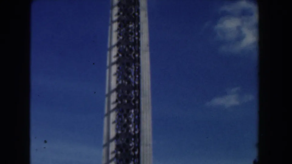 Upward-looking 1961 Nassau home-movie view of the tower shaft against saturated blue sky and light clouds.
