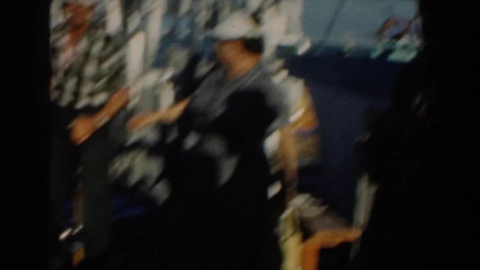 Soft, motion-blurred 1961 Nassau frame showing adults in hats moving near the hanging fish display beside the boat.