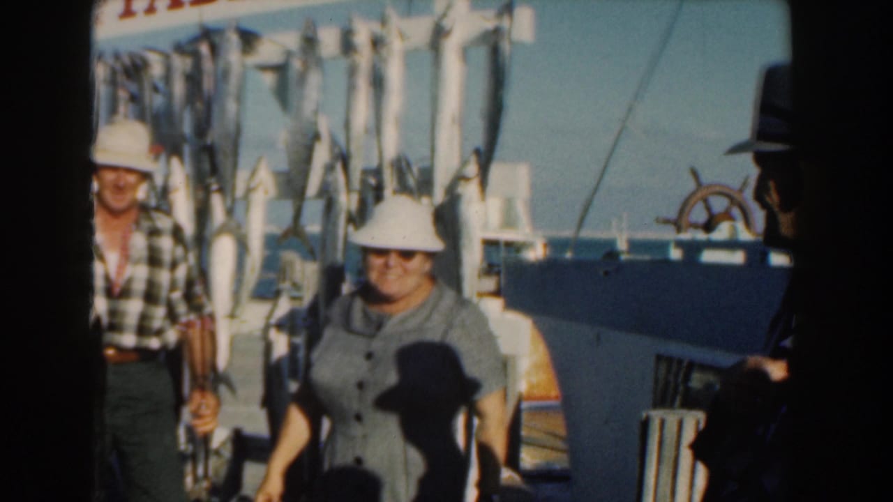 Adults on a boat deck stand beside a rack of hanging fish and a Pablo II sign.