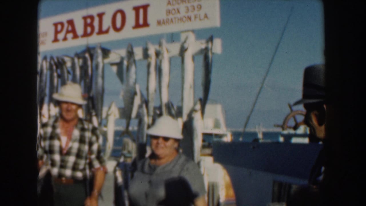 Two adults in white hats stand beside hanging fish on the Pablo II boat.
