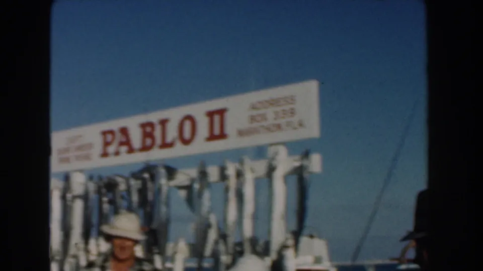 Close 8mm view of the Pablo II boat sign above a rack of fish, with a person in a white hat partly visible below.