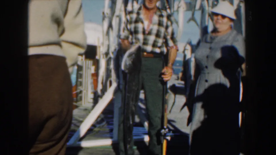 On a Nassau fishing vessel, a man holding a rod and a woman in a gray dress pose beside hanging fish and deck rails.