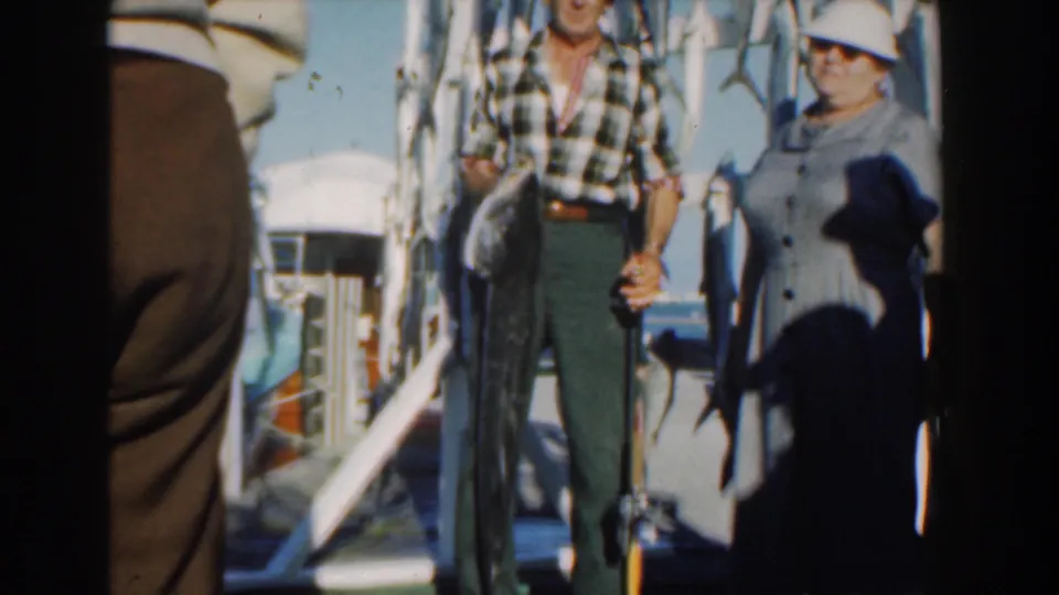 The final frame keeps the Nassau boat scene on the adults and catch, with strong sunlight and a shadow falling across the woman.