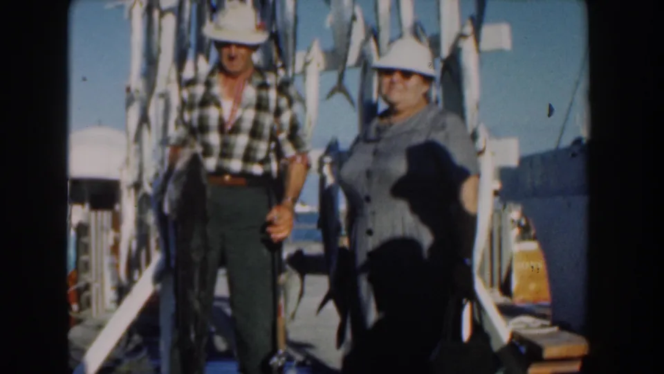 A slightly lower 8mm frame shows the couple on the Nassau dock, the man holding a large fish with more catch hanging nearby.