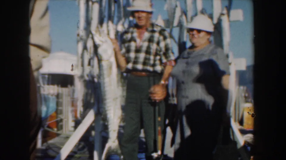 Near the end of the clip, the man holds a long fish prominently while the woman remains beside him on the Nassau dock.