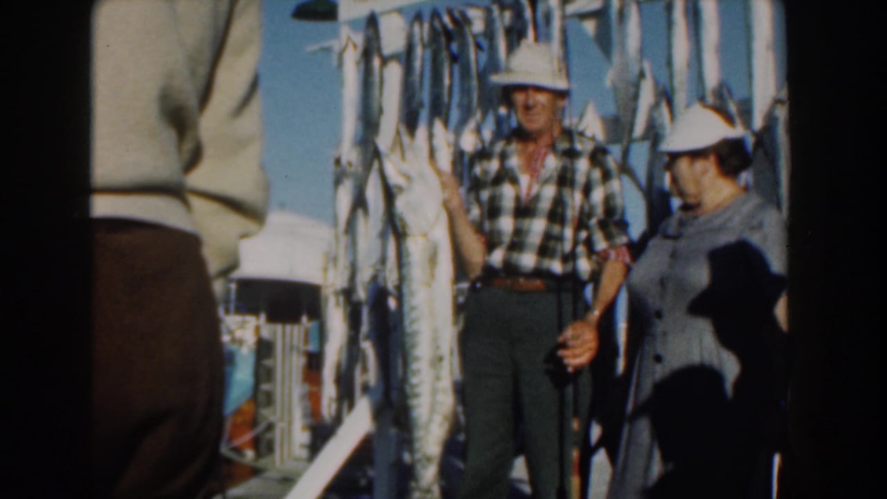 Couple posing on a boat beside a rack of large hanging fish.