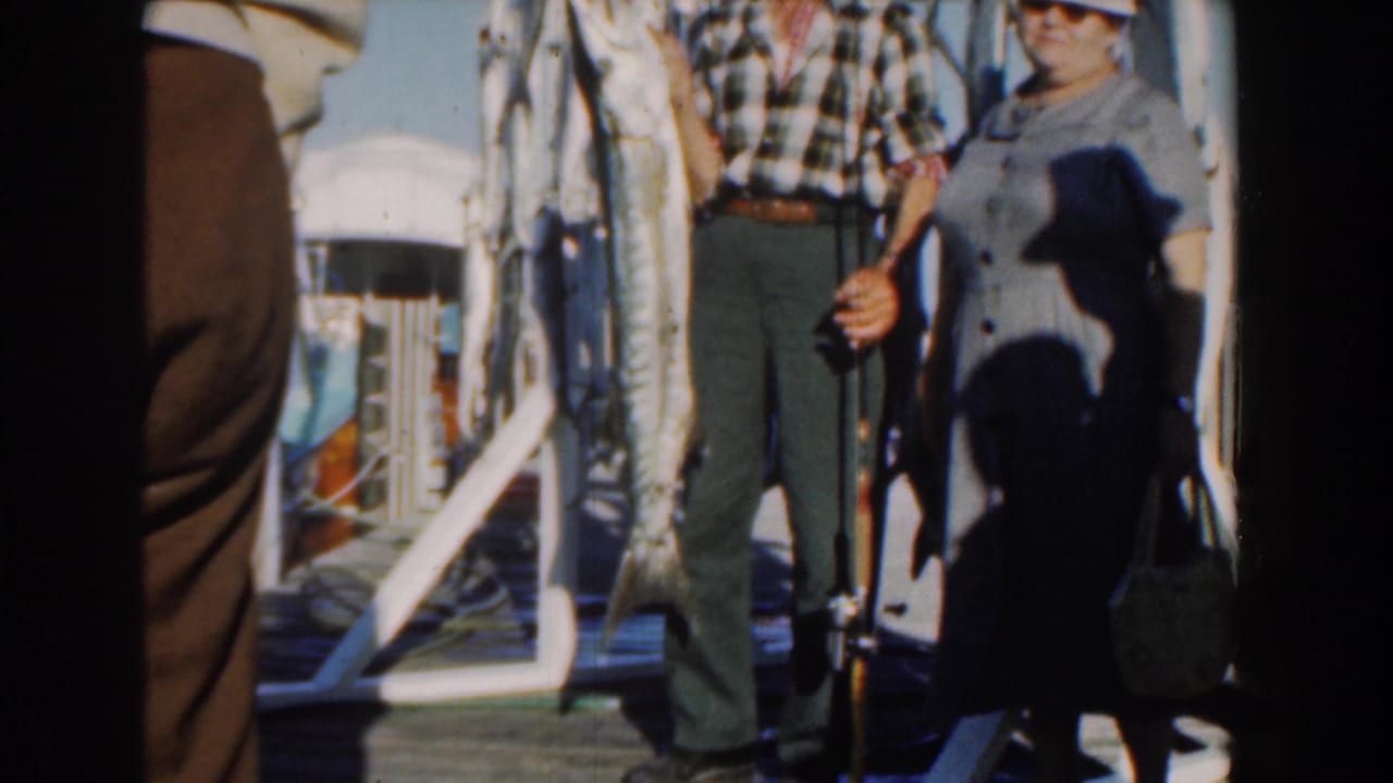 Man and woman on a boat next to hanging fish and a partial sign.