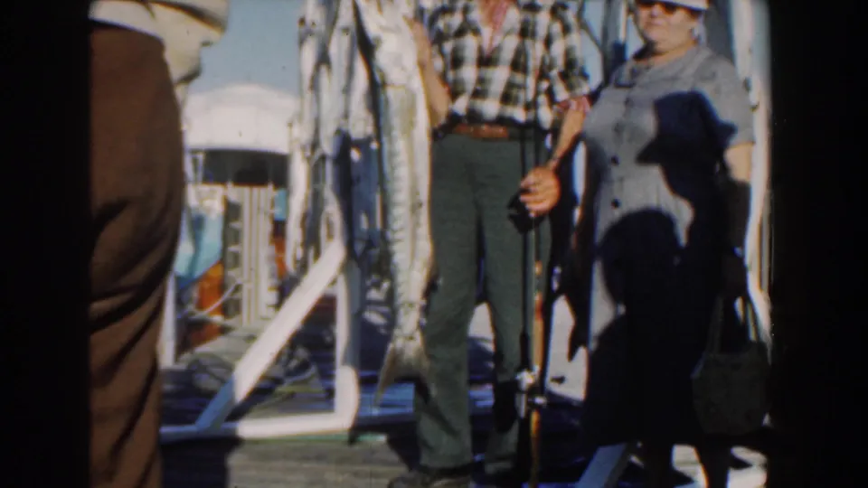 A 1961 Nassau boat scene shows a man and woman near a hanging fish display, with part of a sign and deck equipment visible.