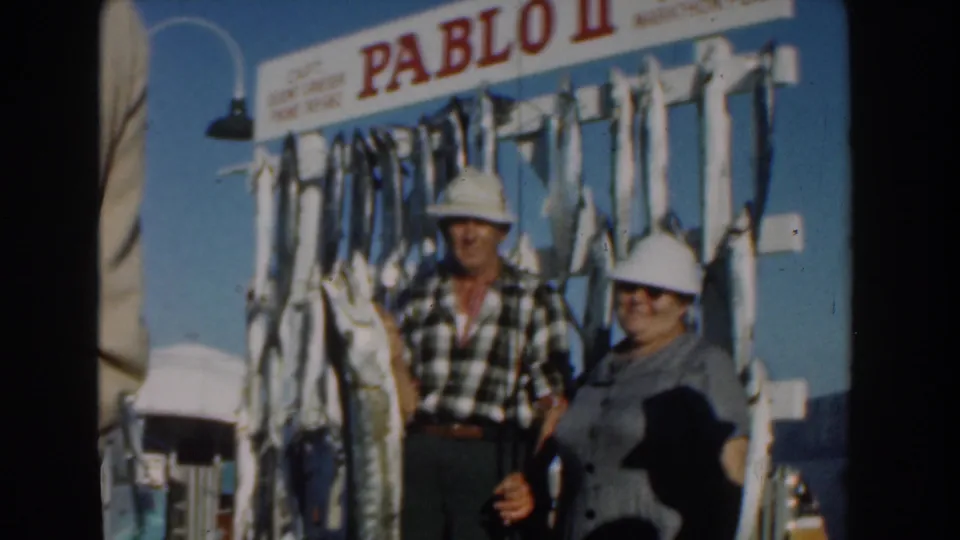 The 1961 Nassau frame shows the couple beside a fish display on a boat, with the PABLO II sign visible over the scene.