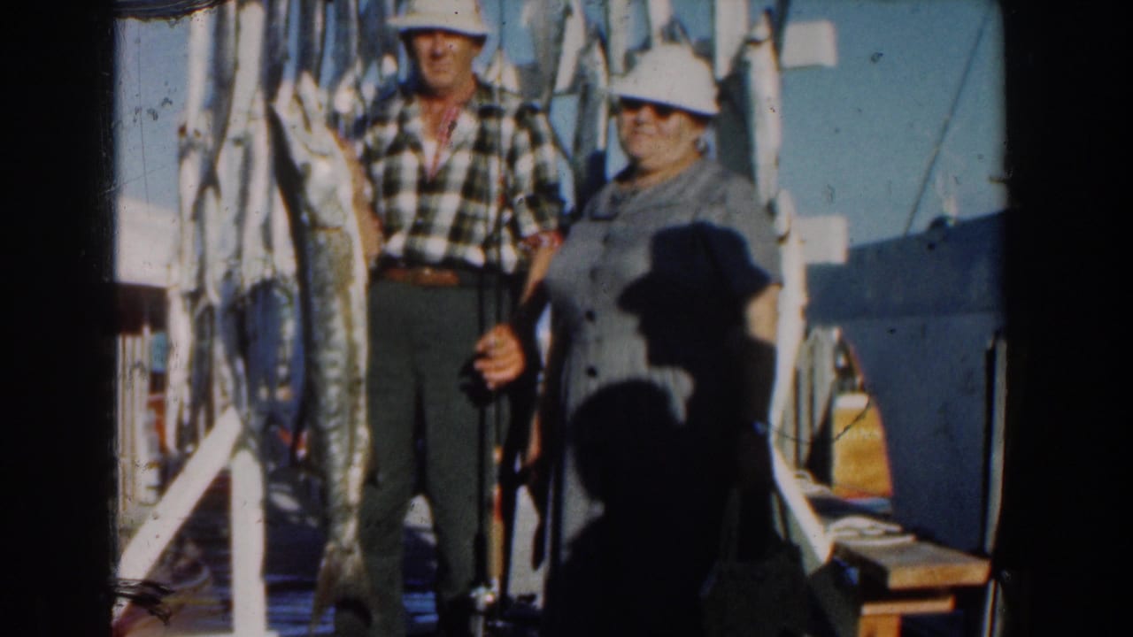 Couple stands on a boat with large fish hanging beside them.
