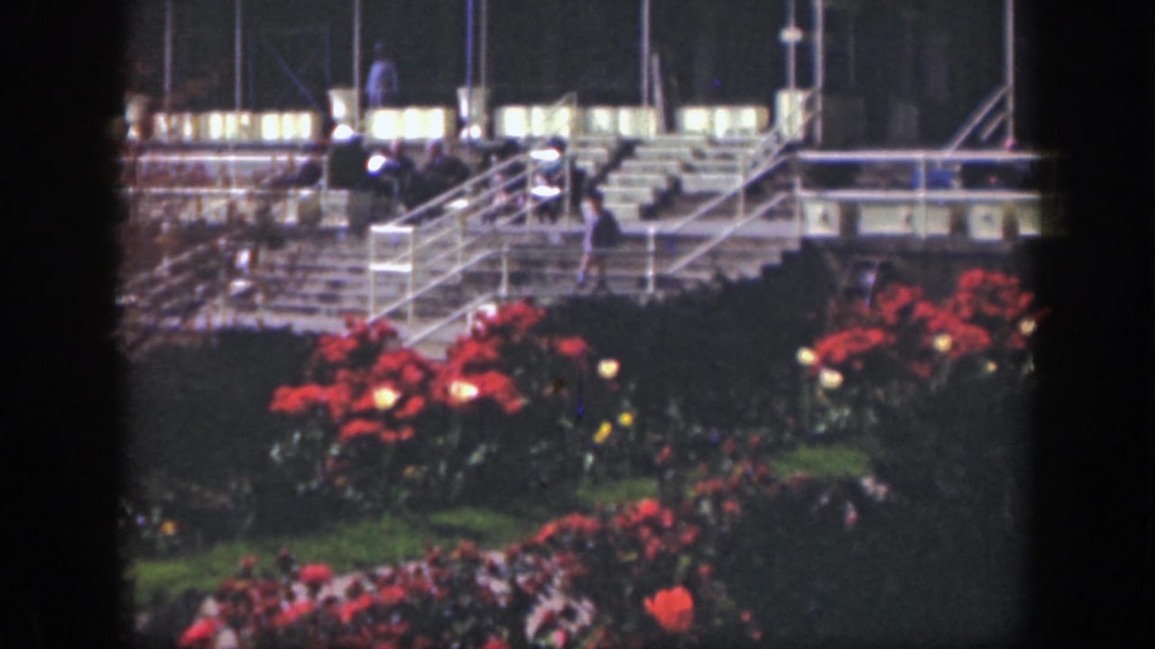 1949 Cincinnati 8mm frame showing red flower beds before illuminated stairs, bleachers, and distant people in an outdoor venue.