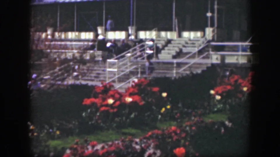 1949 Cincinnati home-movie frame with landscaped red flowers, lit stair rails, tiered seating, and distant figures at night.