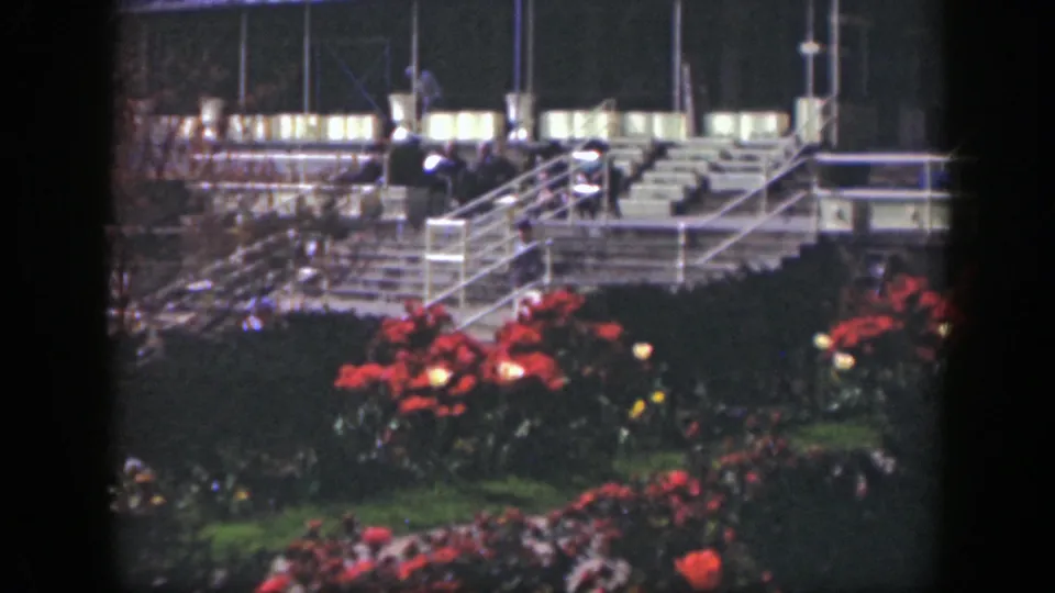 1949 Cincinnati 8mm still of flower plantings in the foreground and distant people moving near lit steps and bleachers.