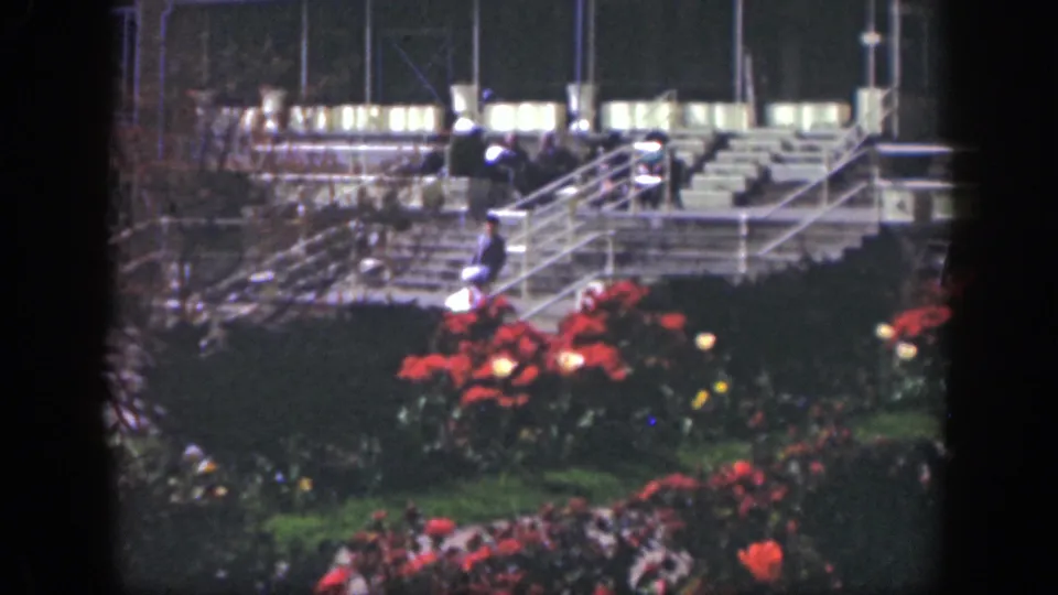 1949 Cincinnati frame showing a distant person descending stairs behind red flower beds in a softly exposed nighttime venue.