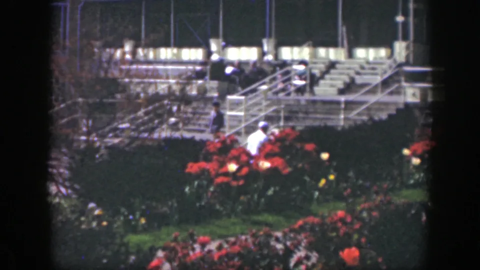 In 1949 Cincinnati home-movie footage, distant visitors move near red flower beds below broad outdoor stairs and white railings.