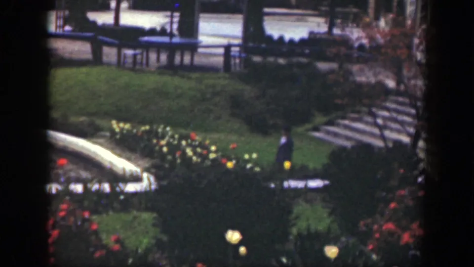 A lone visitor walks below stepped garden paths, benches, lawn, and flower beds in the stated 1949 Cincinnati footage.