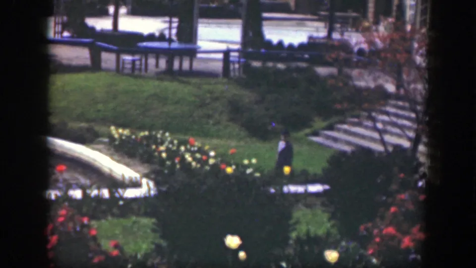 The garden view shows benches, stepped paths, lawn, flowers, and a distant standing figure in the stated 1949 Cincinnati home movie.