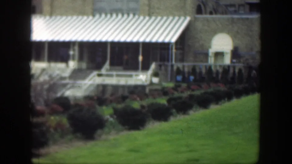 1949 Cincinnati exterior showing striped awnings, a tan brick facade, lawn, shrubs, steps, and a pale arched doorway.