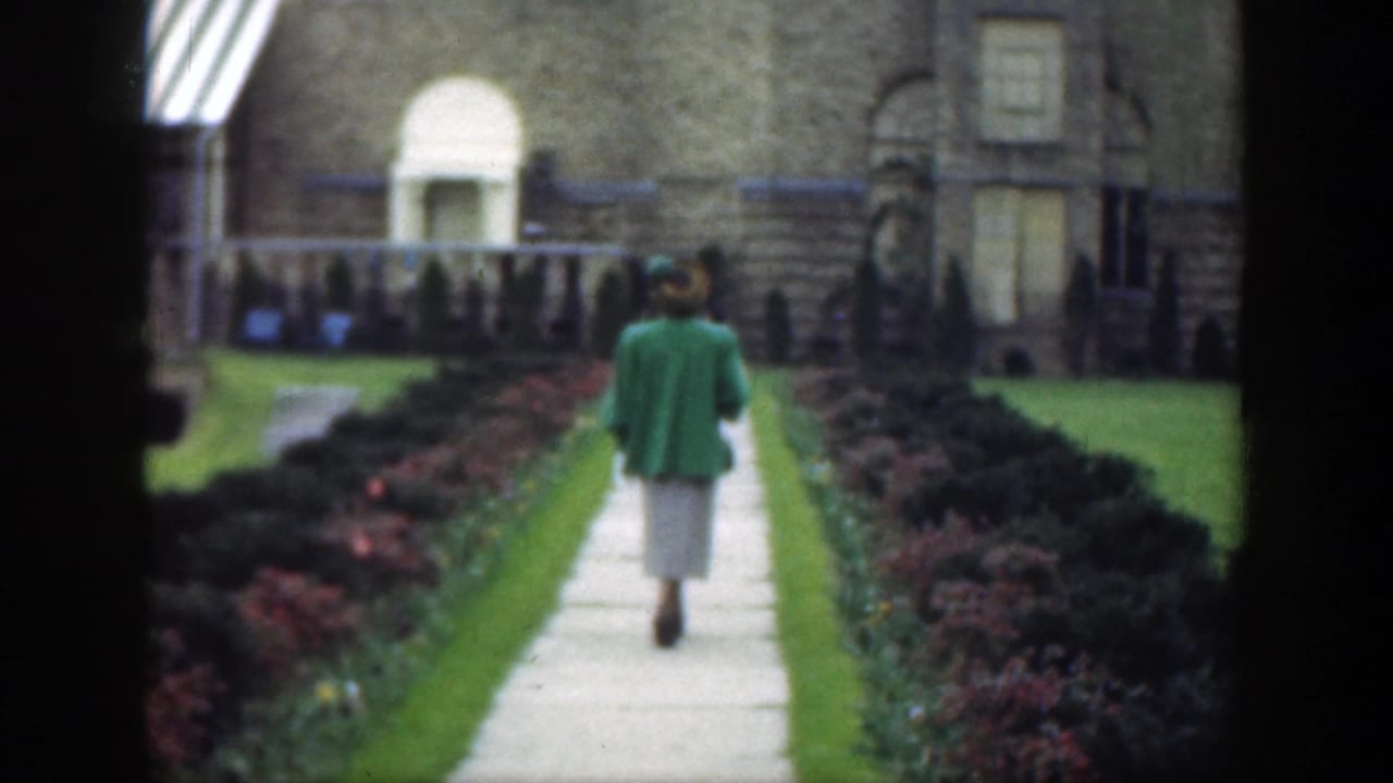 Woman continues down the walkway between hedges and flower beds.