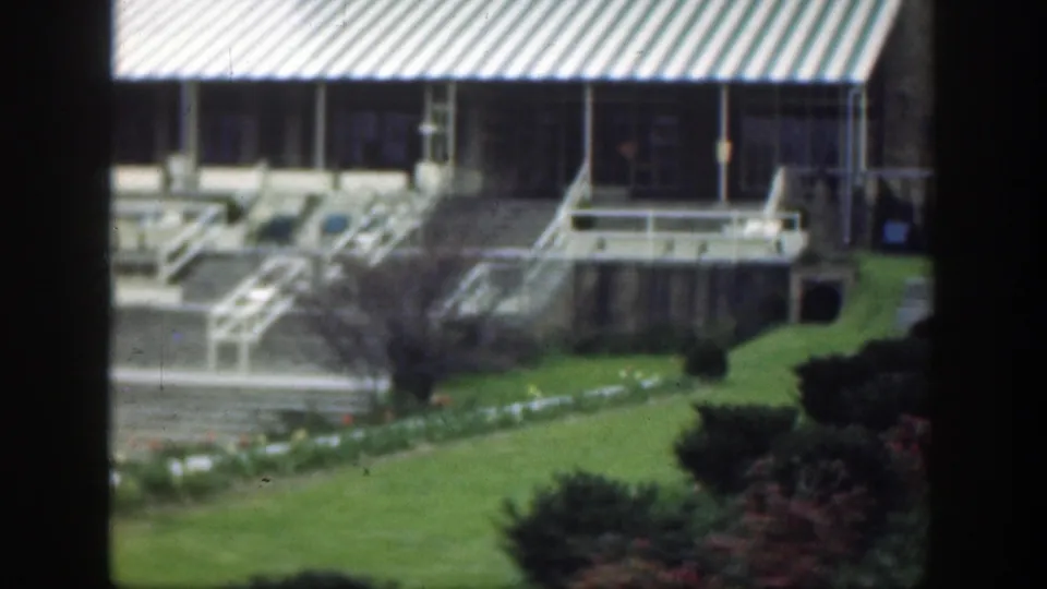 The final frame lingers on the formal grounds, showing lawn, hedges, steps, railings, and a striped awning near a stone building.