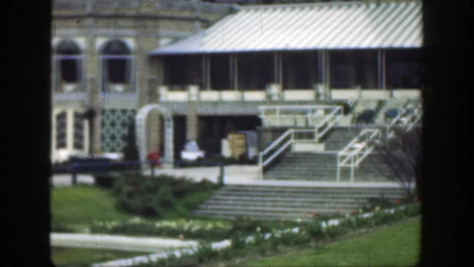 1949 Cincinnati frame with arched windows, striped awning, central steps, railings, lawn, and a walkway across landscaped grounds.