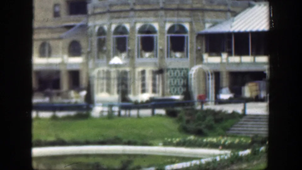 1949 Cincinnati 8mm frame showing arched windows, a sheltered porch, railings, lawn, garden planting, and a curving path.