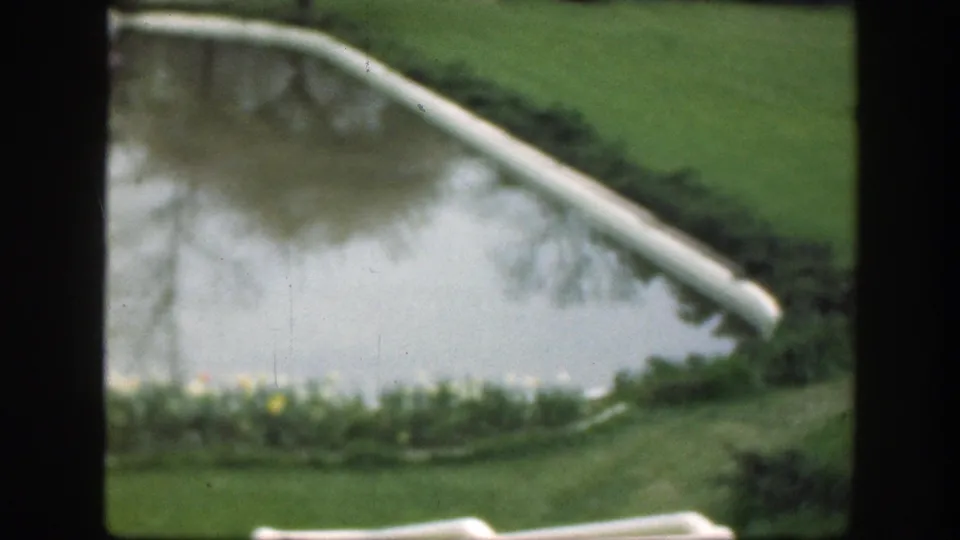 1949 Cincinnati home-movie view of a pond corner with curved edging, green lawn, tree reflections, flowers, and shrubs.