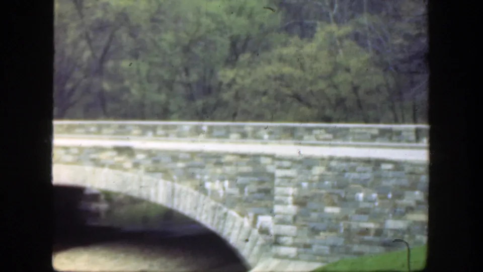 1949 Ohio 8mm frame cropped across the bridge wall and arch, with river water below and trees in the background.