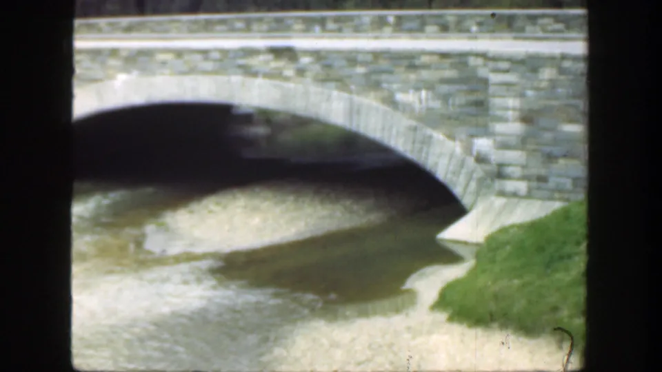 1949 Cincinnati view of the bridge arch, stonework, shallow riverbed, and green grass beside the water.