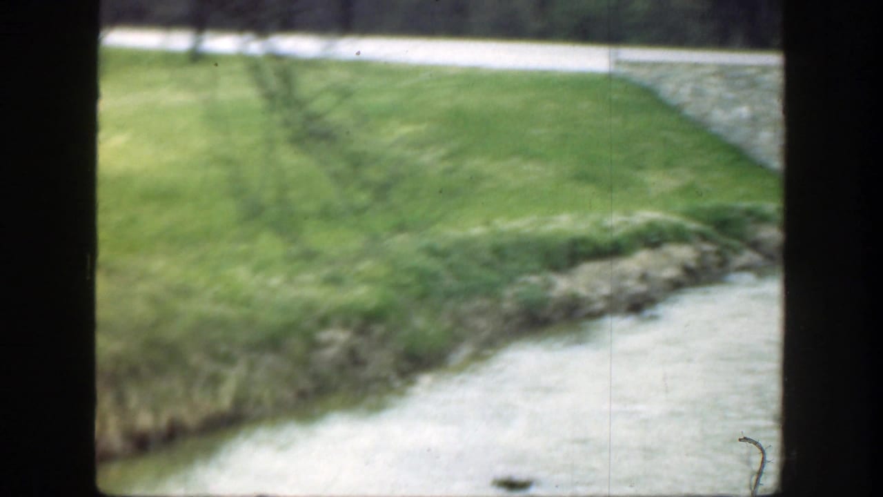 1949 8mm home-movie frame showing grass, a stream or drainage edge, a path, and heavy contact-sheet borders in Ohio metadata context.