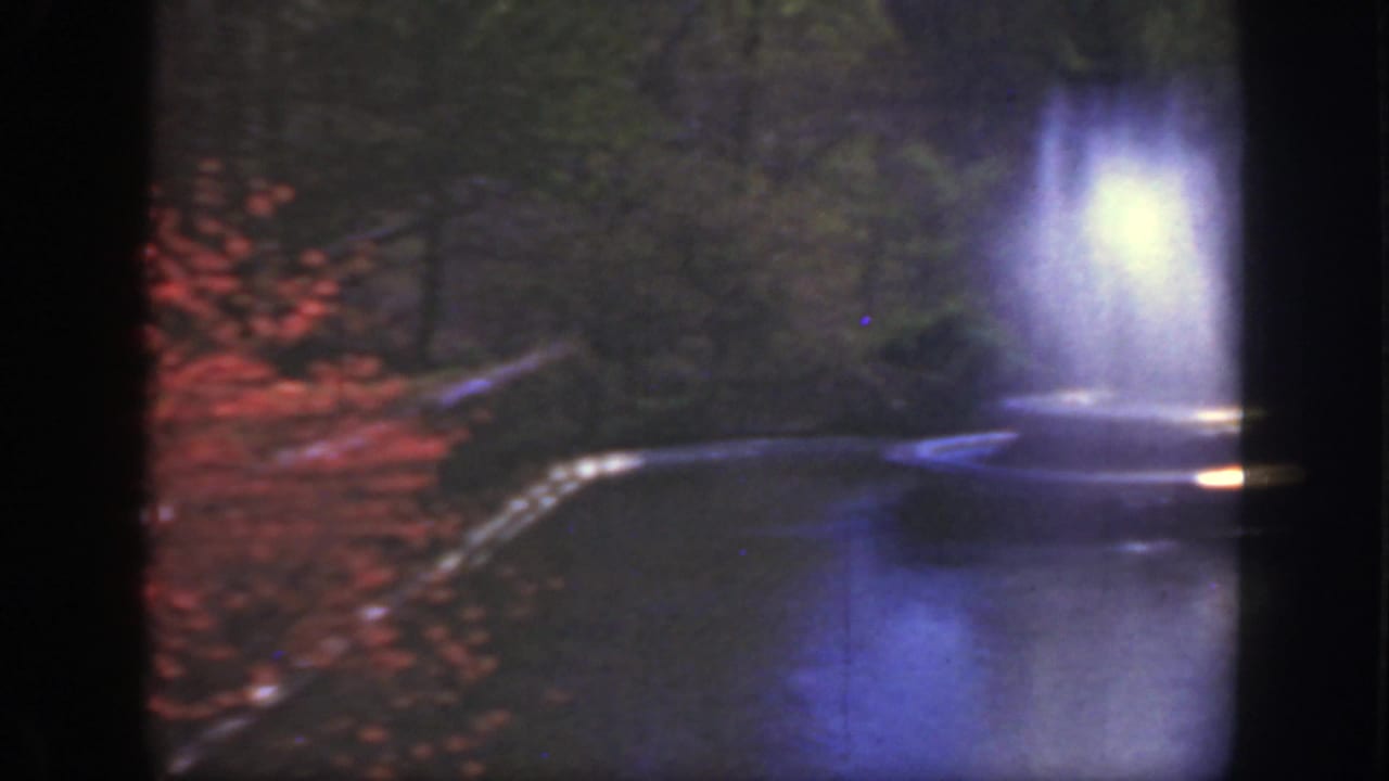 Soft 8mm view of a park fountain spraying water beside trees and a curved basin.