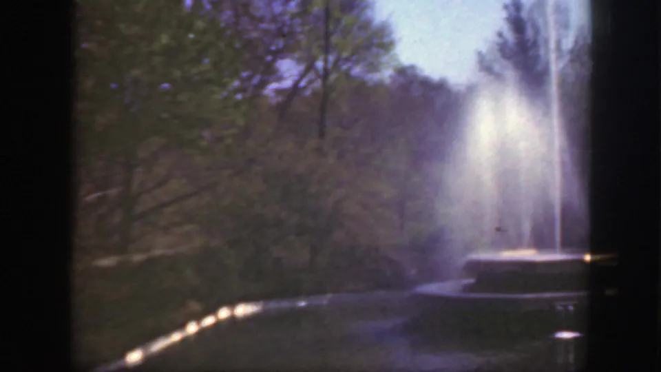 1949 Cincinnati frame showing a circular park fountain, upward water spray, surrounding trees, and soft grainy 8mm color.