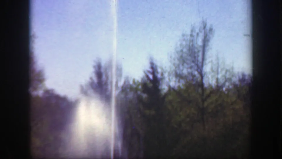 1949 Cincinnati park footage shows a bright vertical beam or spray rising in the distance behind trees under a blue sky.