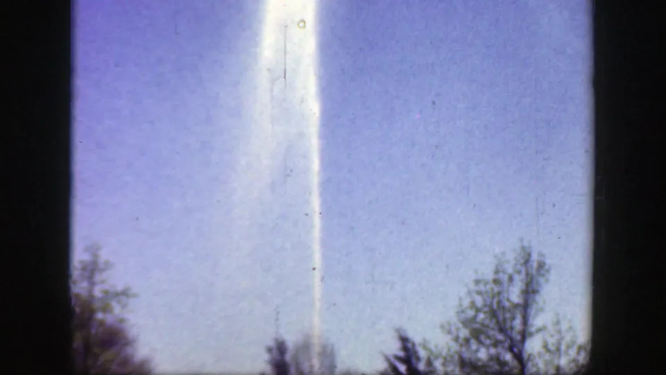 A bright vertical streak fills the 1949 Cincinnati park frame, with tree tops low in view and visible film scratches.