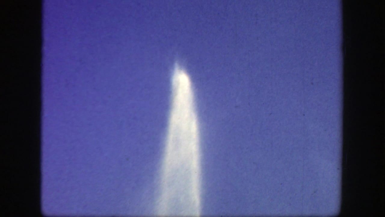 Tall white fountain jet rising against a purple-blue sky within an 8mm frame.